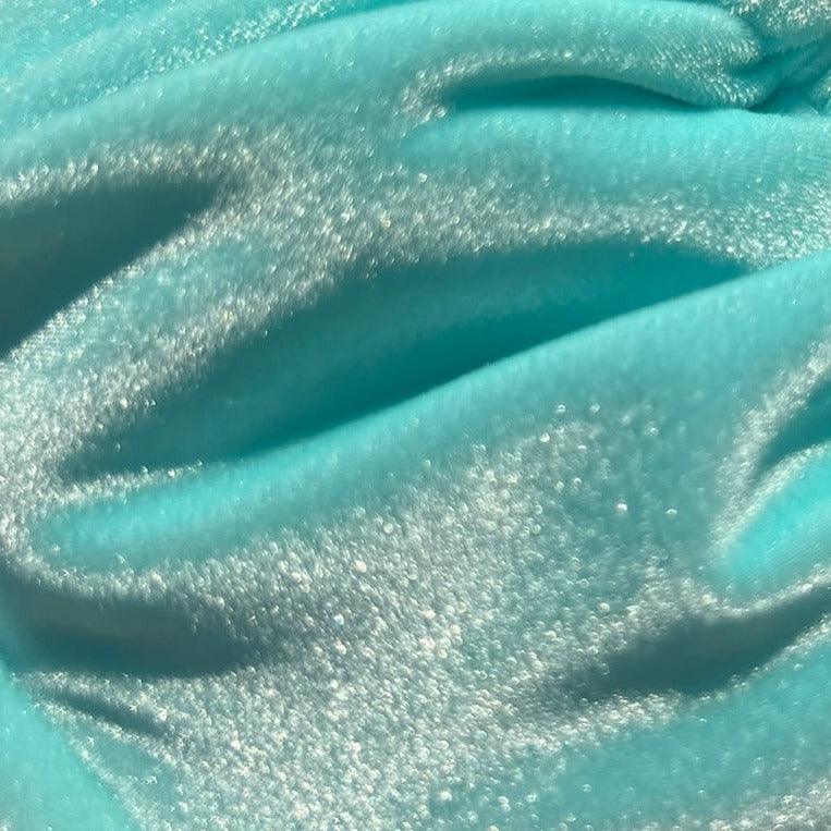 Close up photo of the Vixen, a light blue velvet bikini from Baddie Beach Fantasy Collection, showcasing the iridescence of the fabric in the sun.