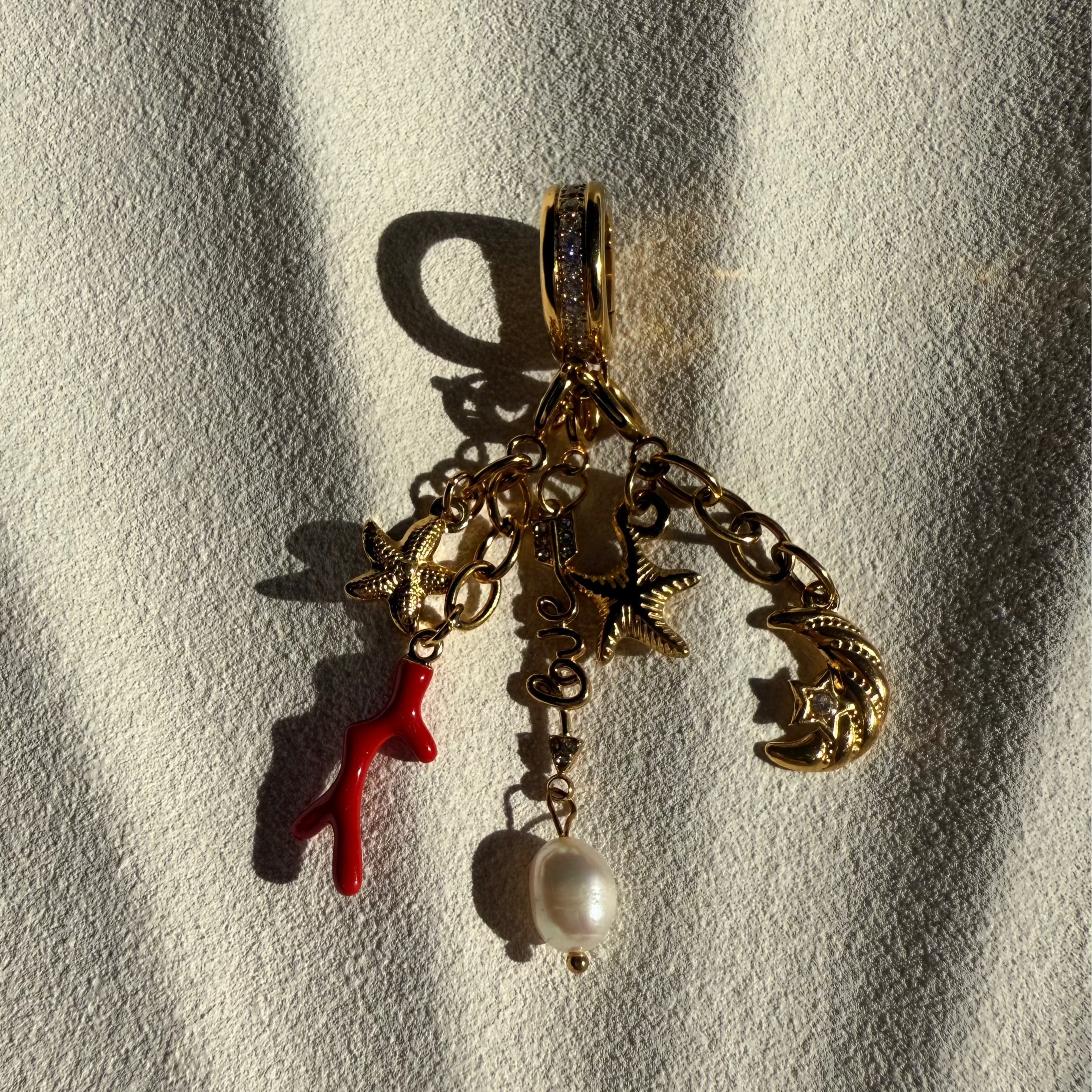 Gold charm with starfish, red coral, and pearl on a textured white background