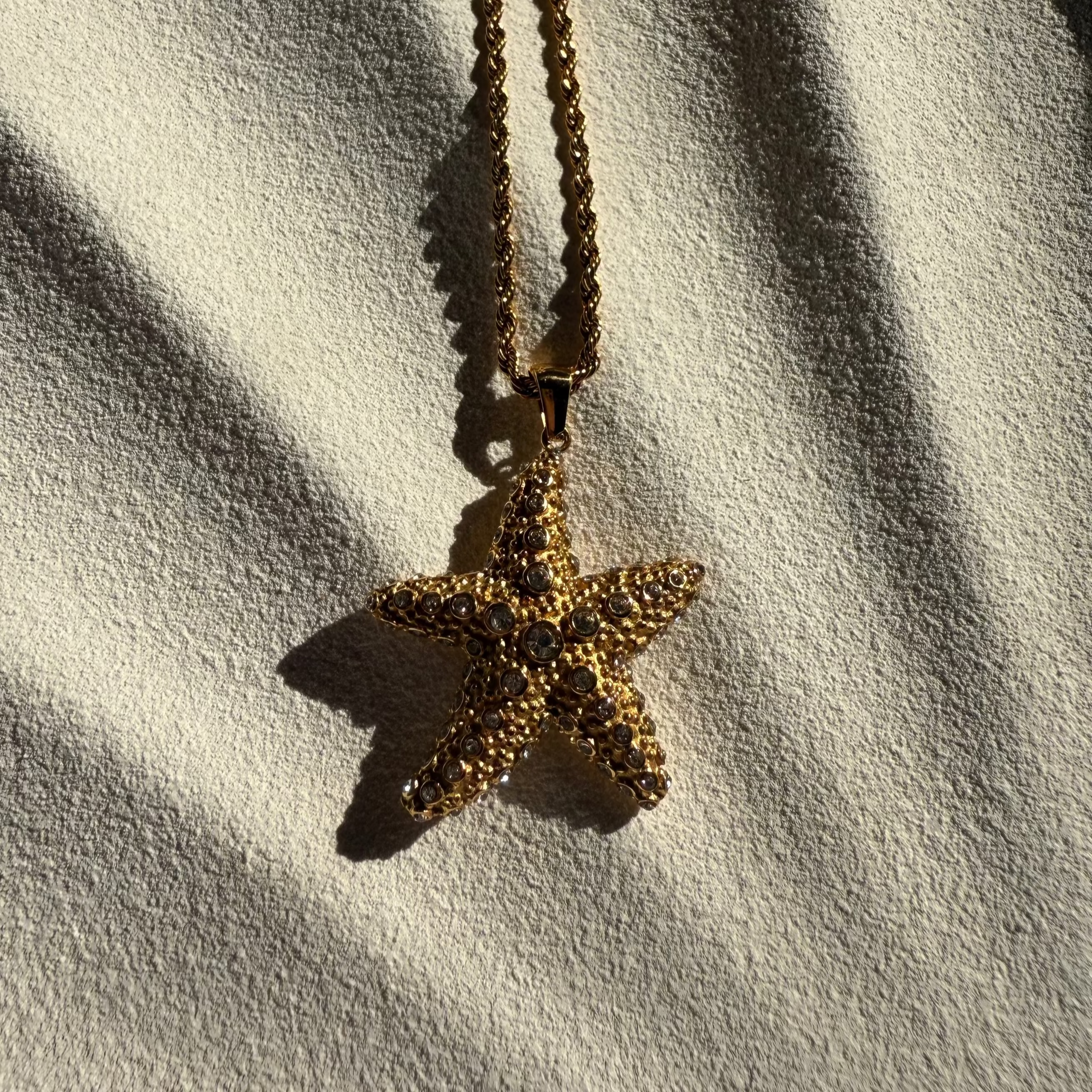 Gold starfish pendant necklace on a white fabric background