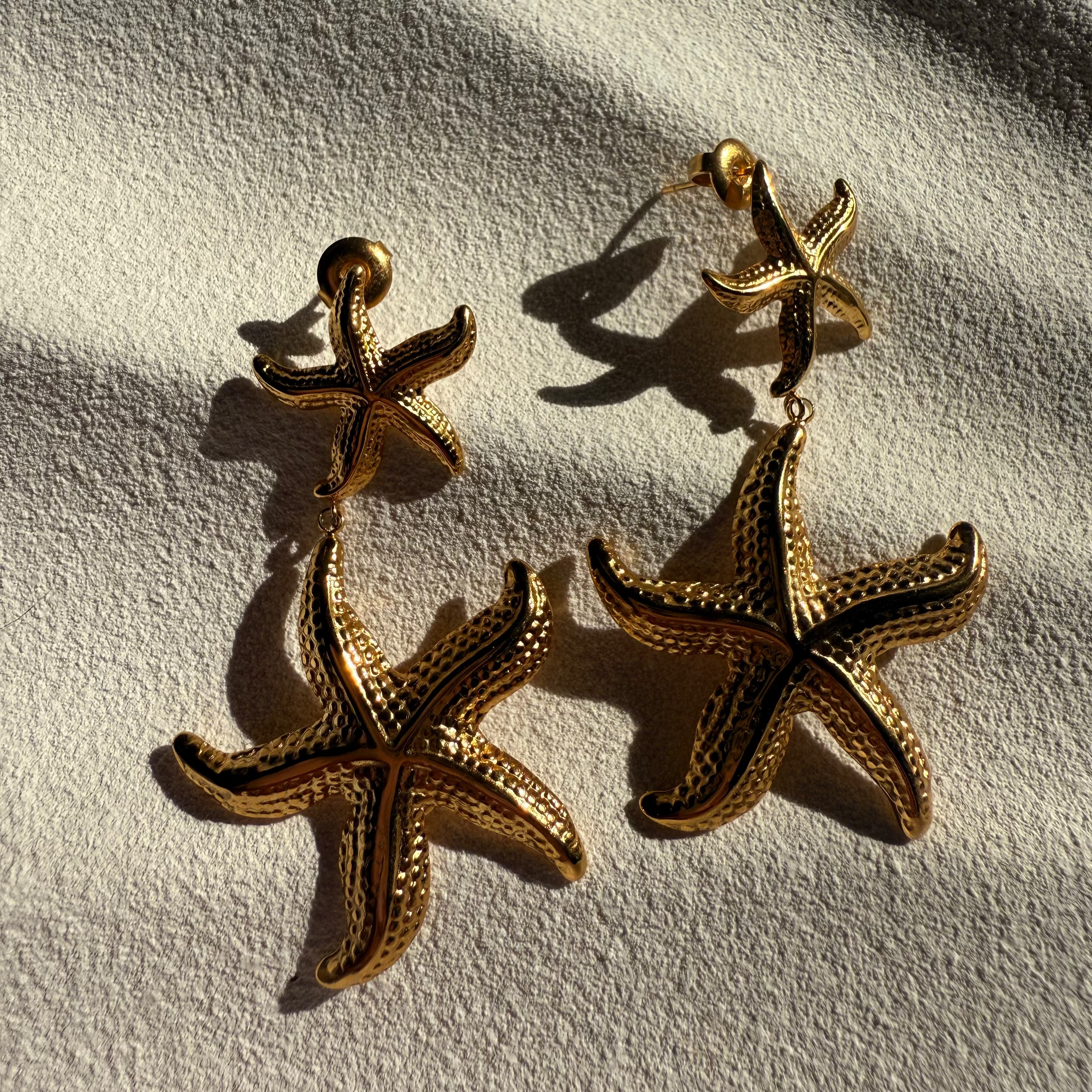 Gold starfish earrings on a textured white surface