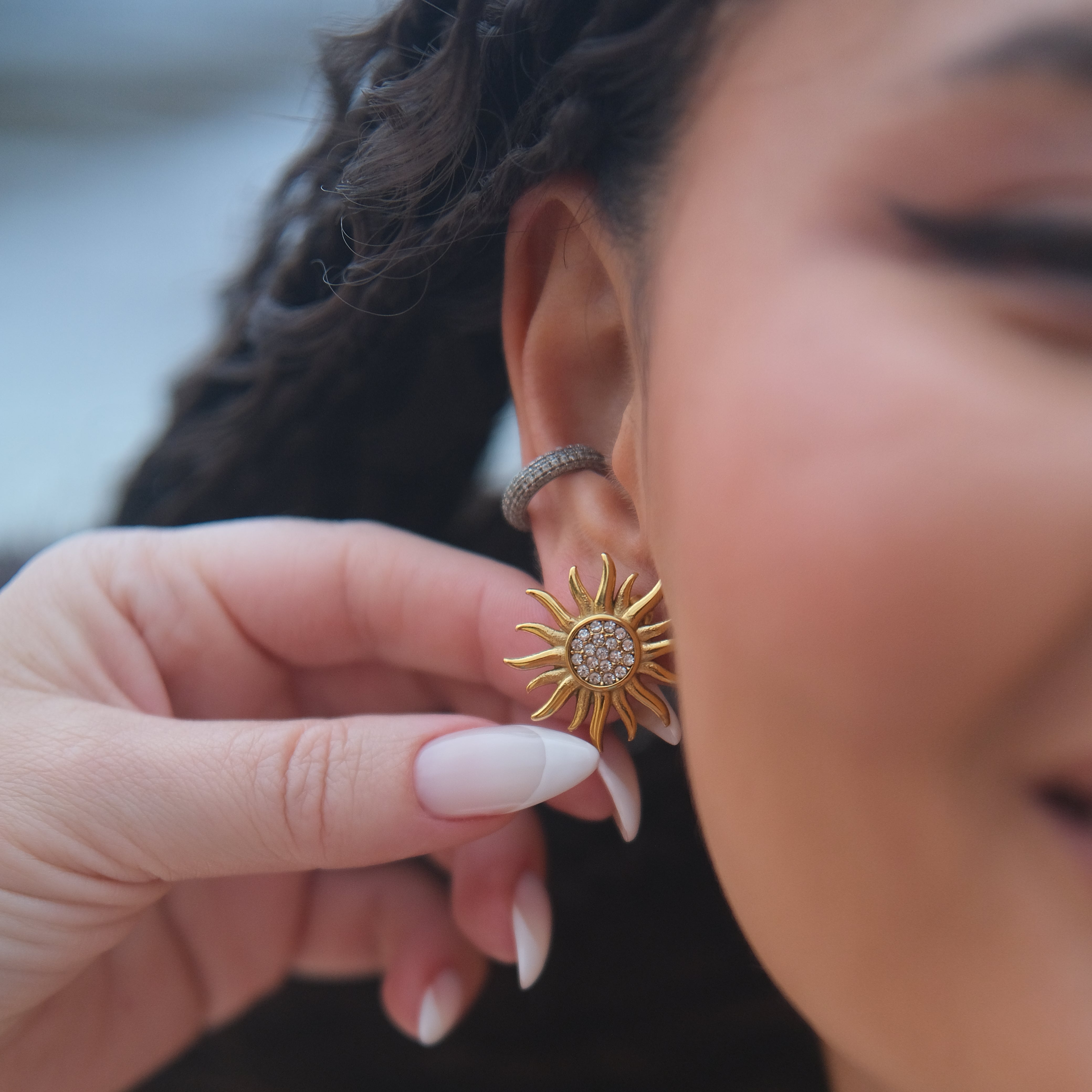 Person wearing a gold sun shaped earring with a blurred background